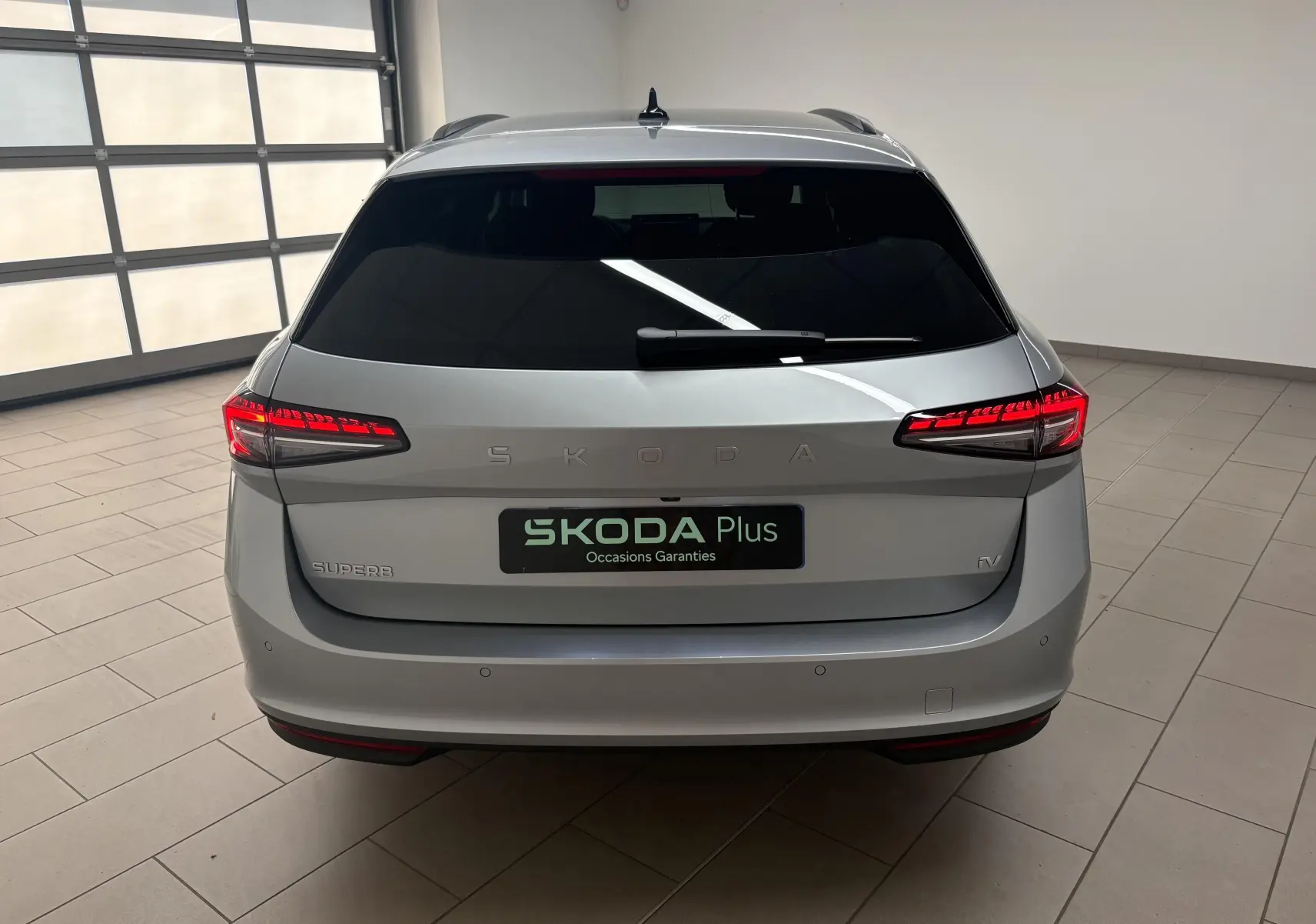 Vue arrière d'une Skoda Superb Combi gris argent avec feux LED allumés dans un garage lumineux.