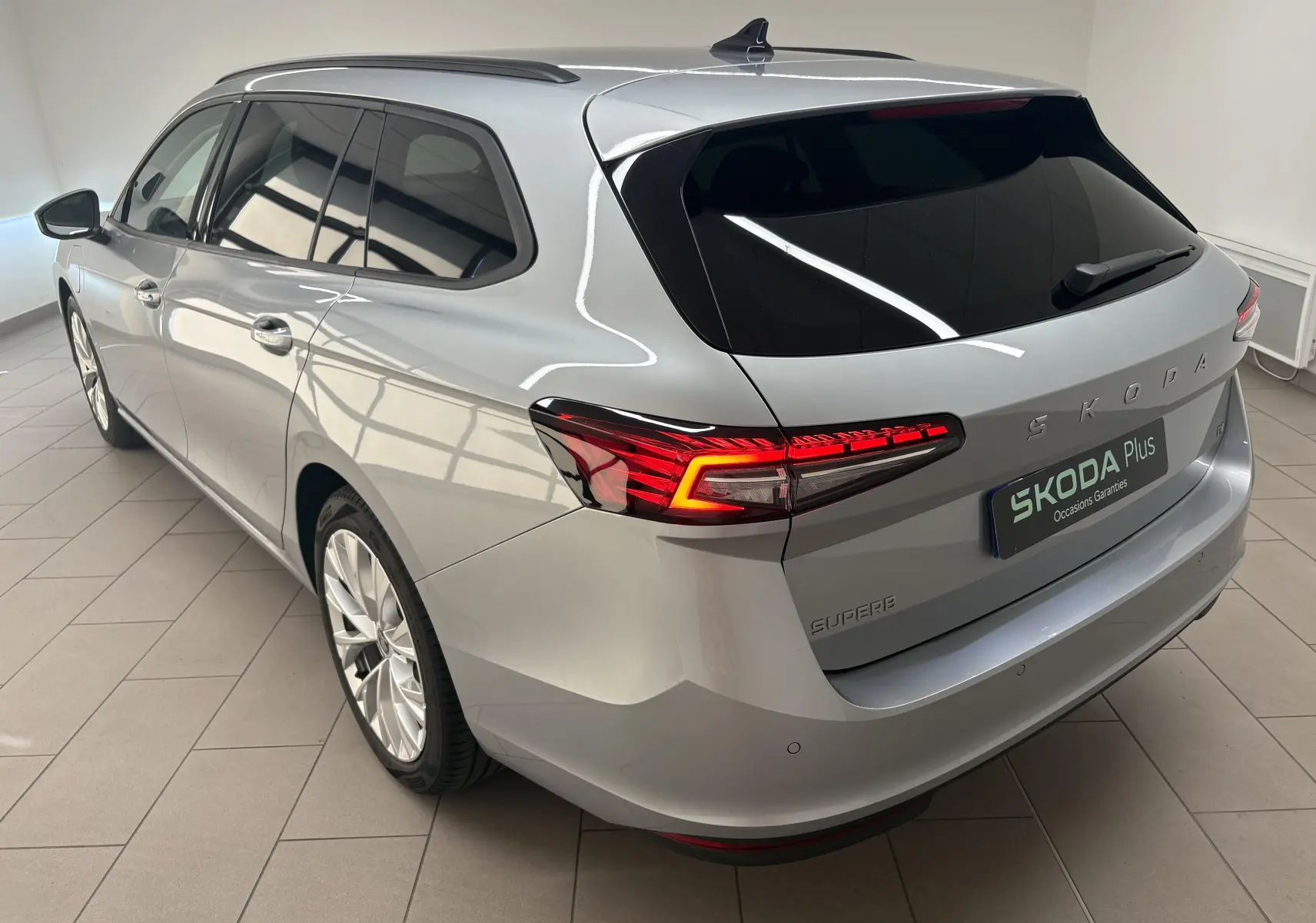 Vue 3/4 arrière droite d'une Skoda Superb Combi gris argent avec feux LED et jantes alliage 18 pouces.