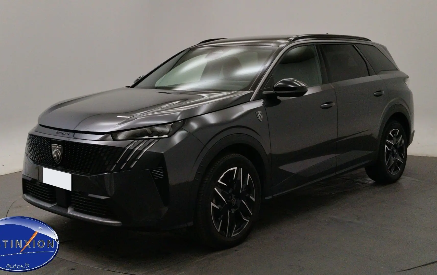 Peugeot 5008 gris titane en 3/4 avant droit, avec jantes noires et phares LED allumés, en showroom.