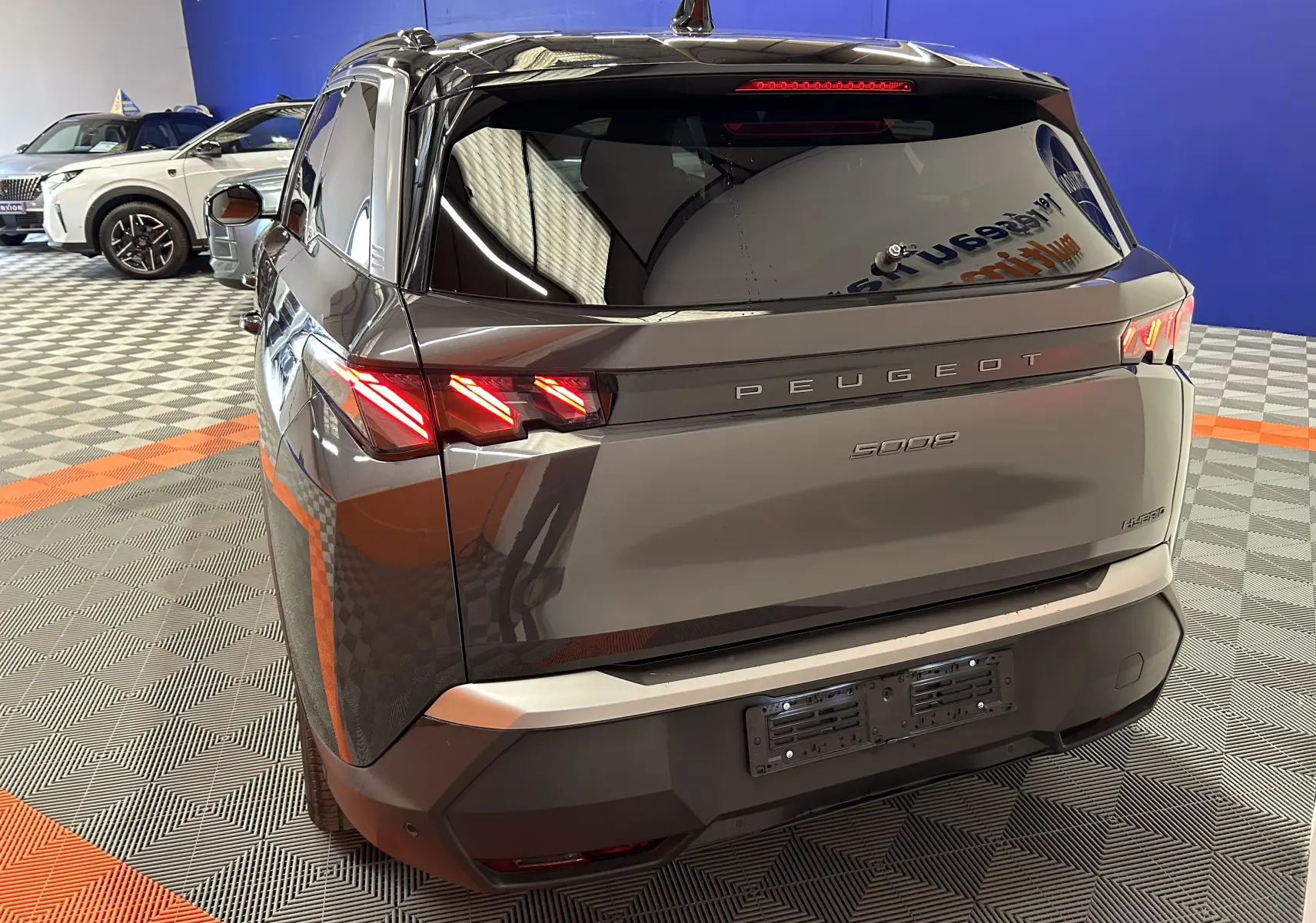 Vue 3/4 arrière droite du Peugeot 5008 gris titane avec feux arrière LED allumés dans un showroom.
