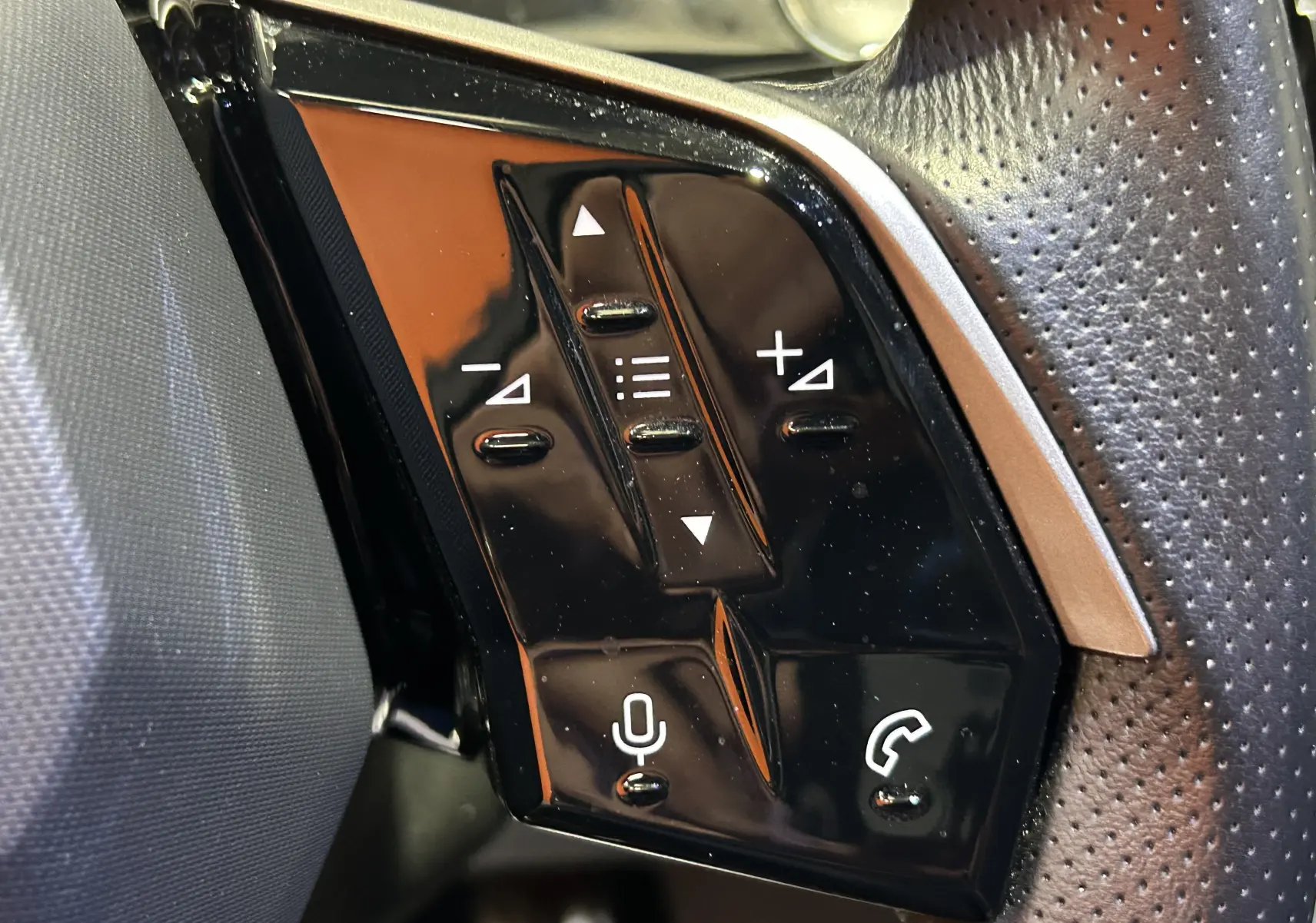 Gros plan sur les commandes noires du volant perforé côté gauche du Peugeot 5008 gris Titane, version hybride 2025.