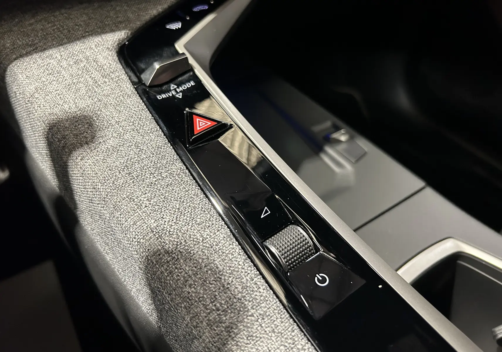 Gros plan sur la console centrale intérieure du Peugeot 5008 III Hybrid 145 GT, tissu gris et commandes noires brillantes.