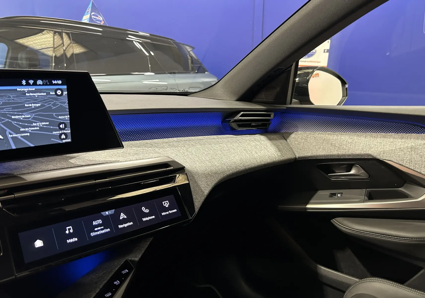 Vue intérieure côté passager du Peugeot 5008 III Hybrid gris titane, avec éclairage d'ambiance bleu et écran tactile central.
