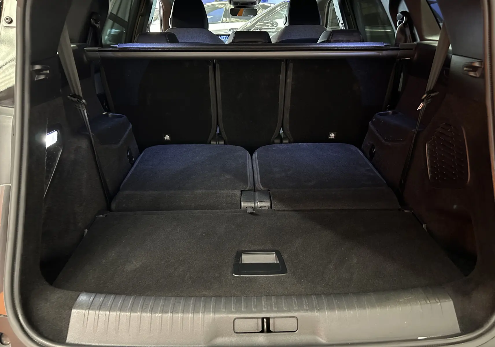 Coffre ouvert vu de l'arrière du Peugeot 5008 gris titane, sièges arrière rabattus pour un grand espace de chargement.