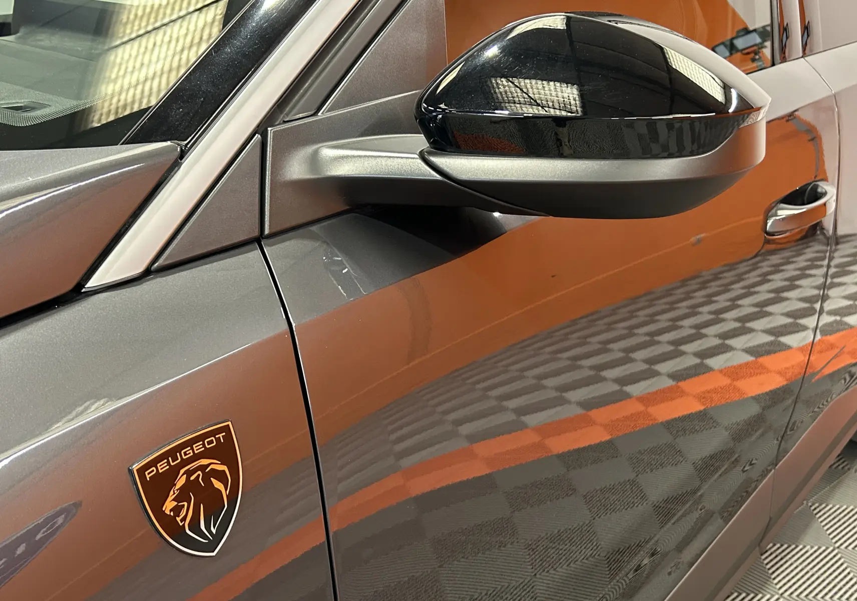 Détail du côté gauche d’un Peugeot 5008 gris titane, avec rétroviseur noir brillant et logo Peugeot lion visible.