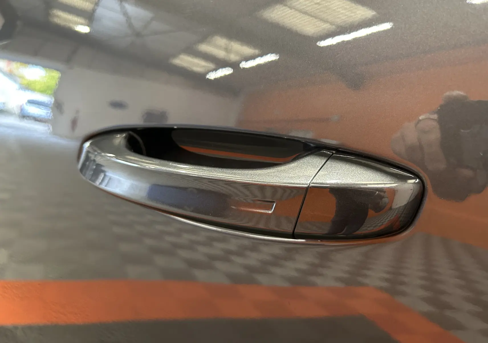Poignée de porte gris titane métallisée du Peugeot 5008 III Hybrid 145 vue en gros plan avec reflet intérieur.