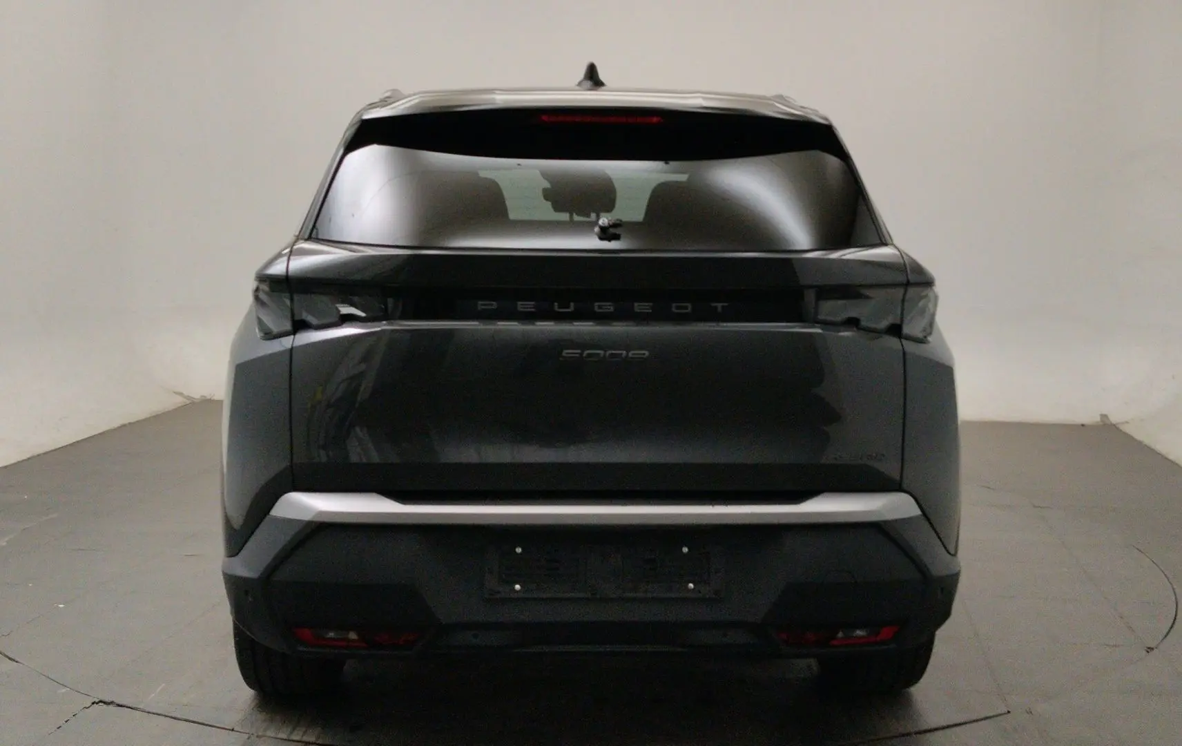 Peugeot 5008 III Hybrid gris titane en 3/4 avant droit, avec phares LED allumés et jantes noires biton.