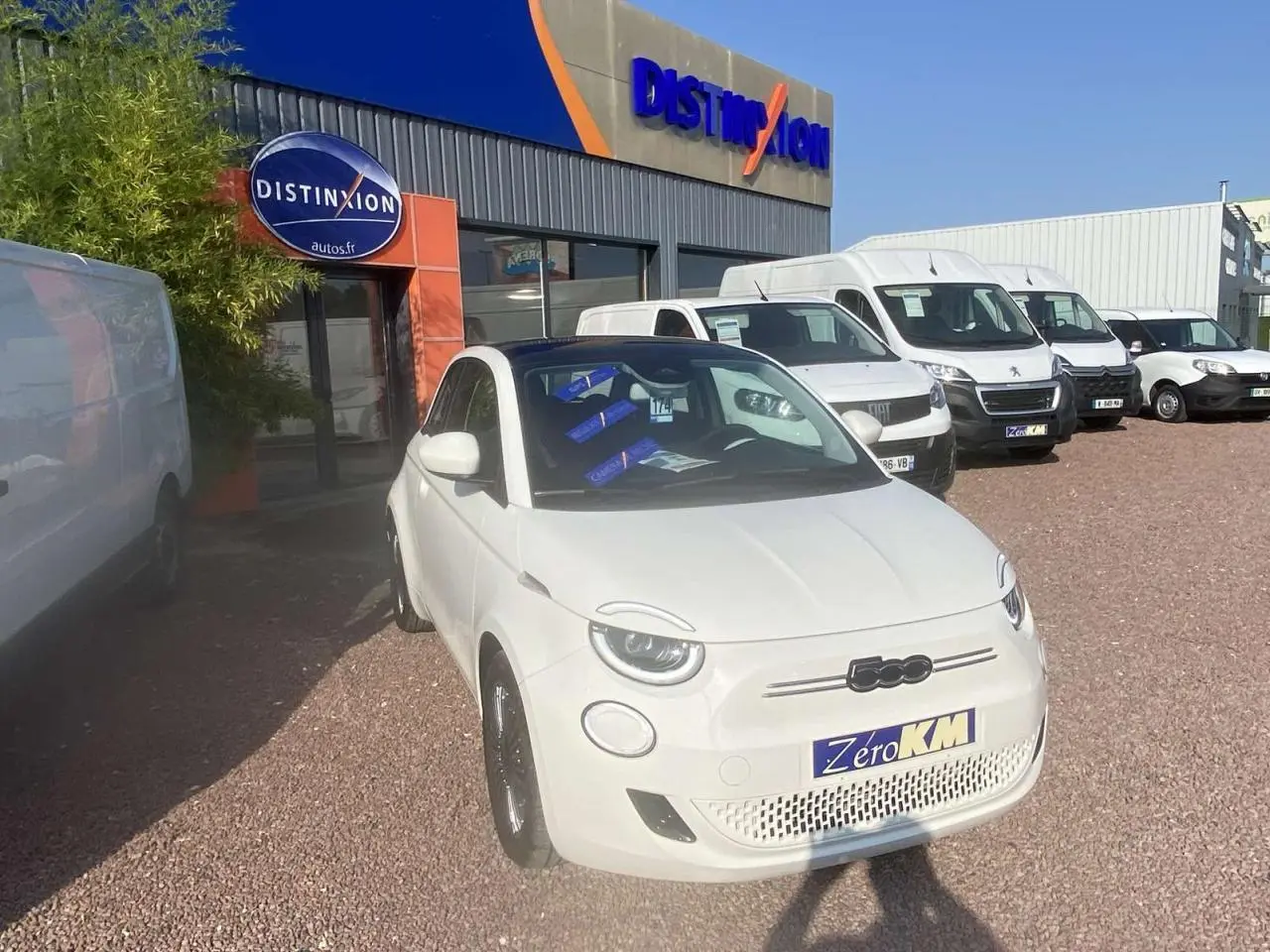 Vue 3/4 avant droite d'une Fiat 500 électrique blanche Ice White avec toit panoramique et jantes noires.