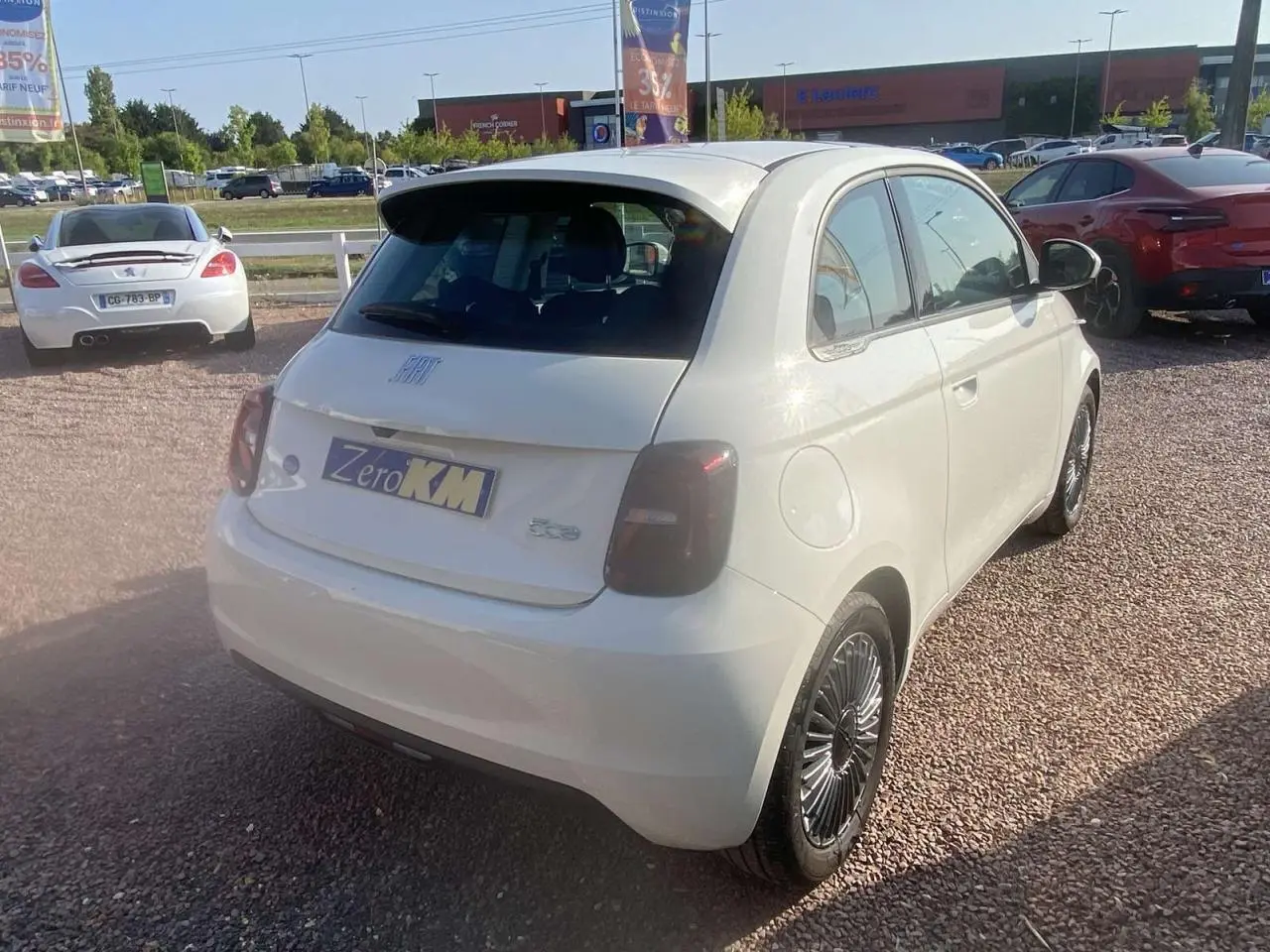 Vue 3/4 arrière droite d'une Fiat 500 électrique blanche avec feux arrière fumés et jantes noires stylisées.