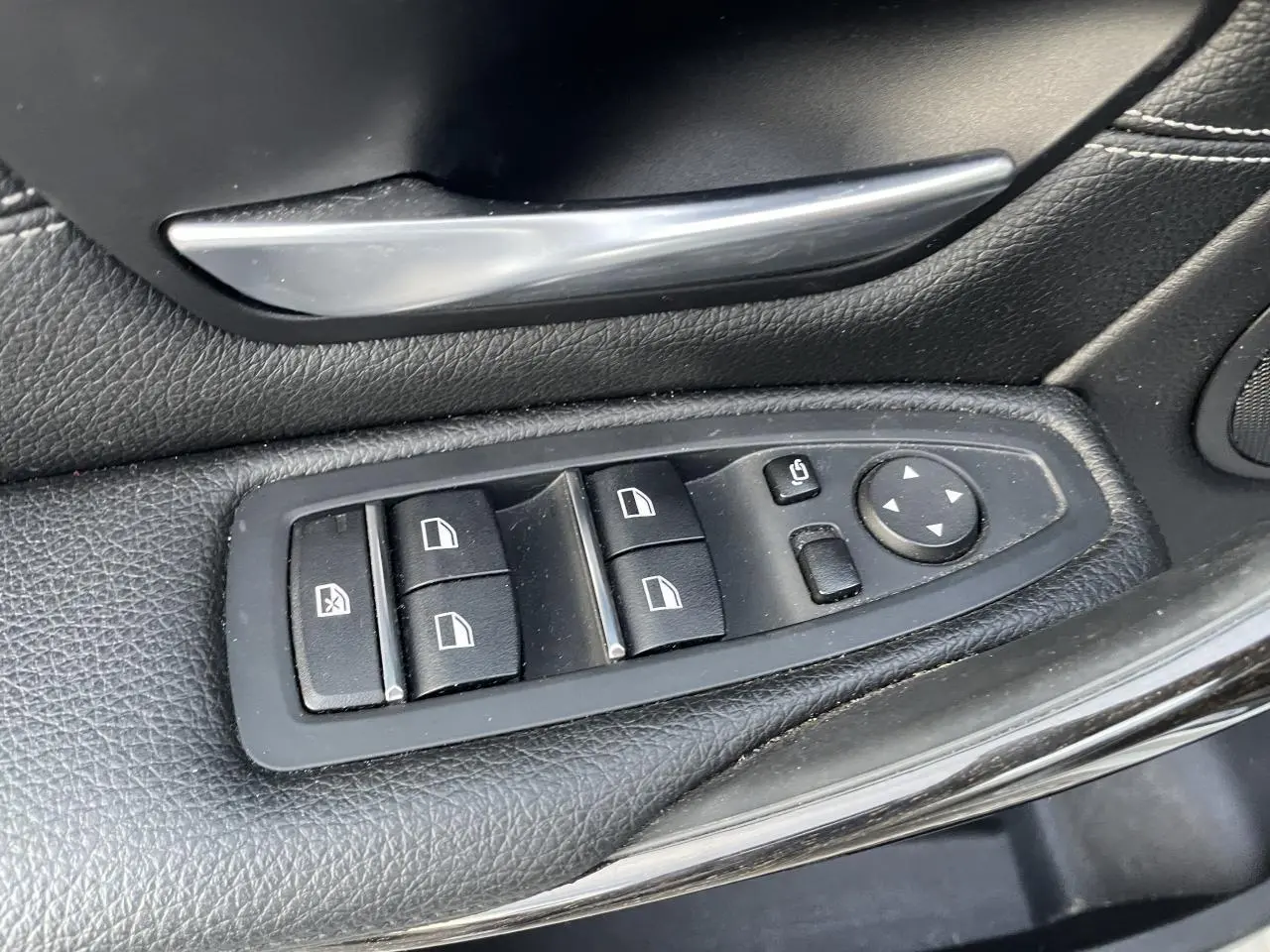 Gros plan sur les commandes de lève-vitres et rétroviseurs côté gauche en cuir noir d'une BMW Série 3 F30 330i xDrive Luxury.