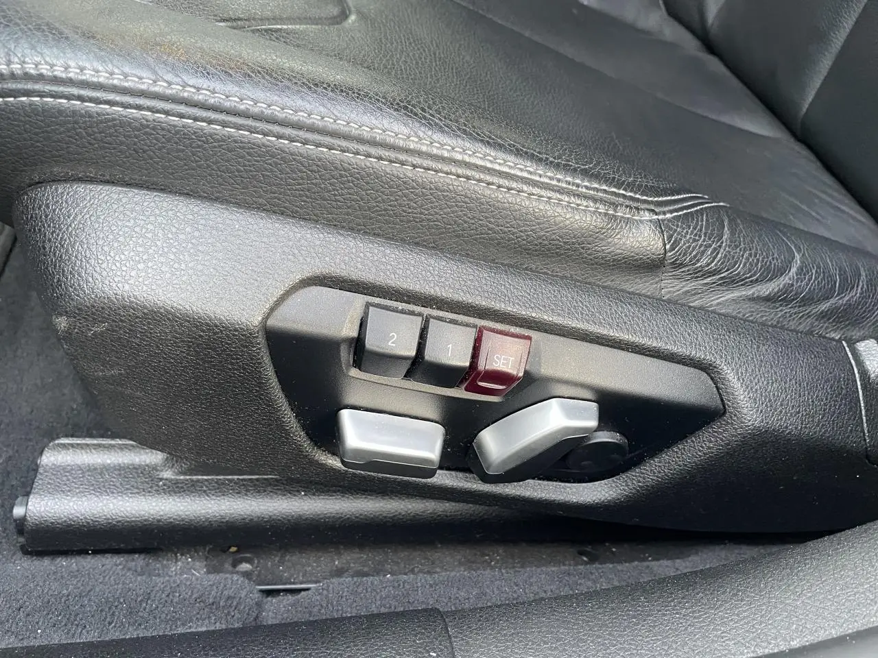 Détail des commandes de réglage électrique du siège conducteur en cuir noir d'une BMW Série 3 F30 330i xDrive.