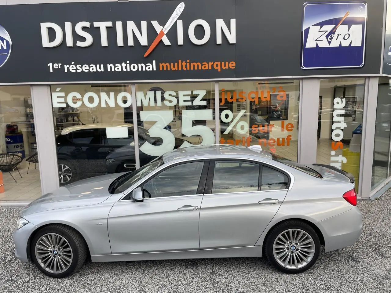 BMW Série 3 F30 330i xDrive Luxury gris clair vue profil côté gauche devant une vitrine avec enseigne Distinxion