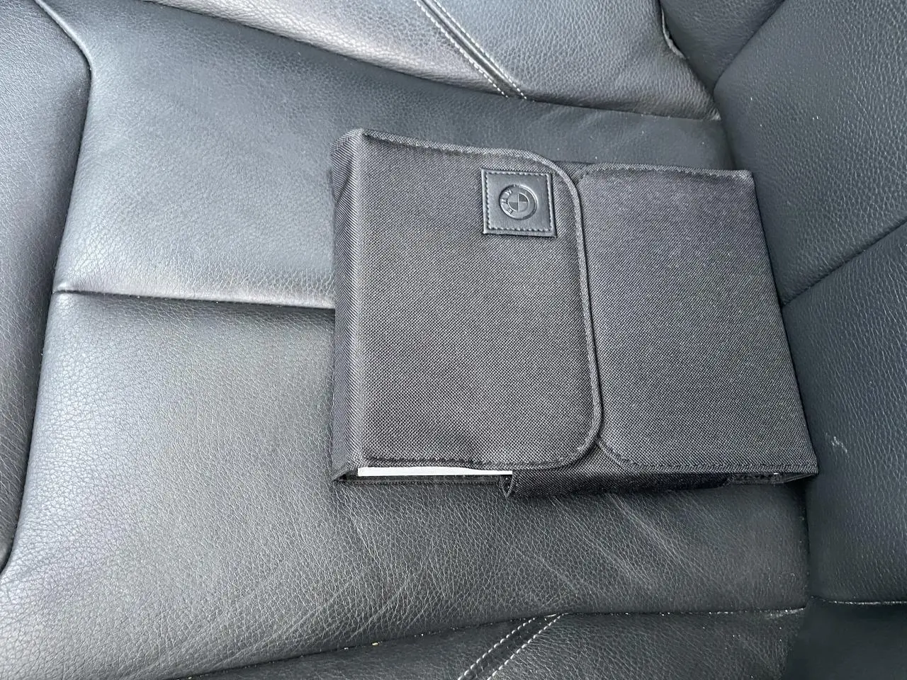 Pochette noire avec logo BMW posée sur la sellerie cuir noire du siège avant d'une BMW Série 3 F30.