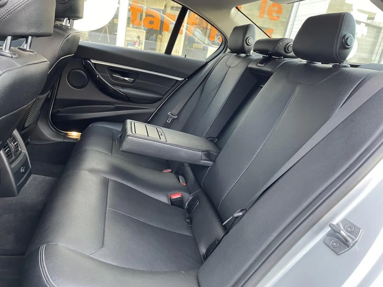 Vue intérieure côté droit de la banquette arrière en cuir noir avec accoudoir central relevé d'une BMW Série 3 F30 gris clair.