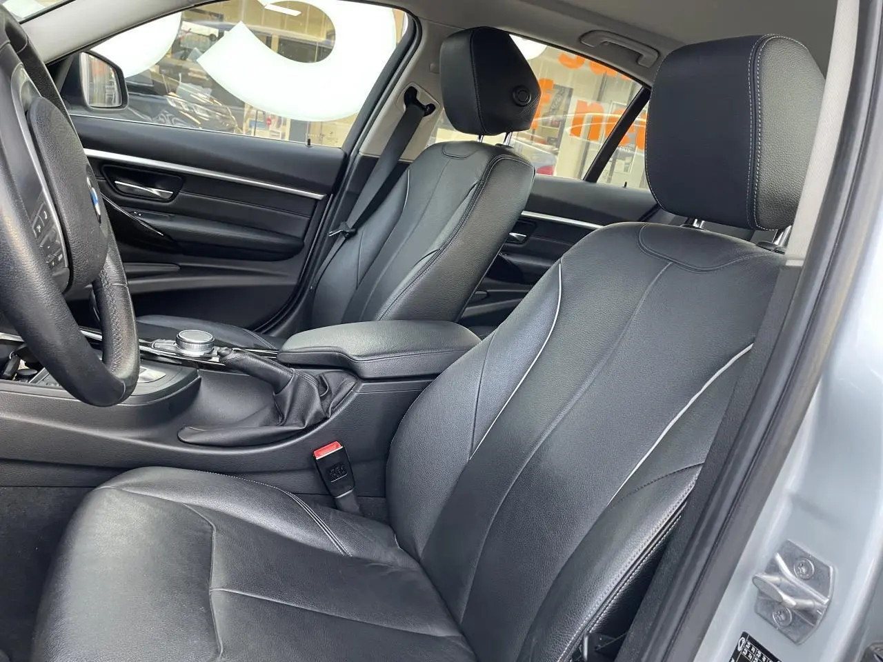 Intérieur avant droit de BMW Série 3 F30 gris clair avec sièges cuir noirs et accoudoir central coulissant.