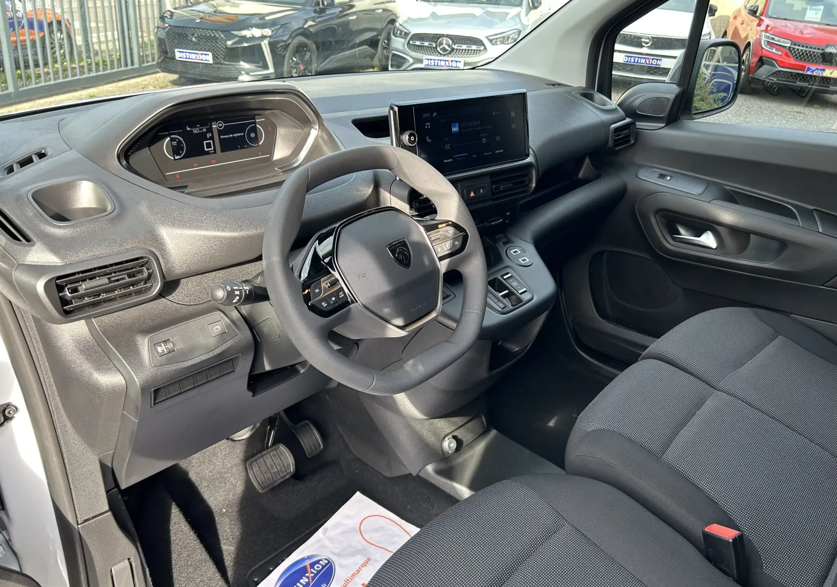 Intérieur du Peugeot Partner Fourgon 2025 vu côté conducteur, tableau de bord moderne avec écran tactile et volant compact noir.