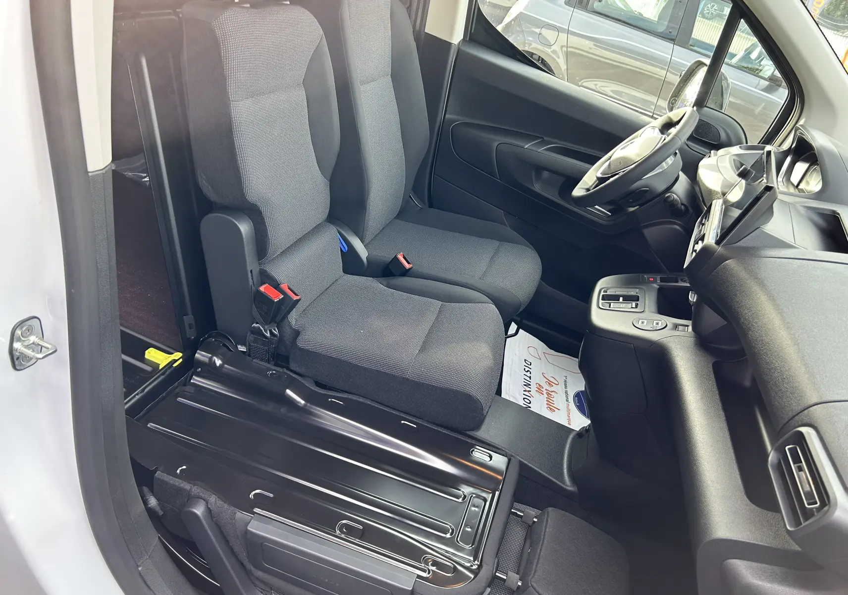 Vue intérieure côté conducteur du Peugeot Partner Fourgon blanc 2025, sièges tissu gris et plancher bois visible.