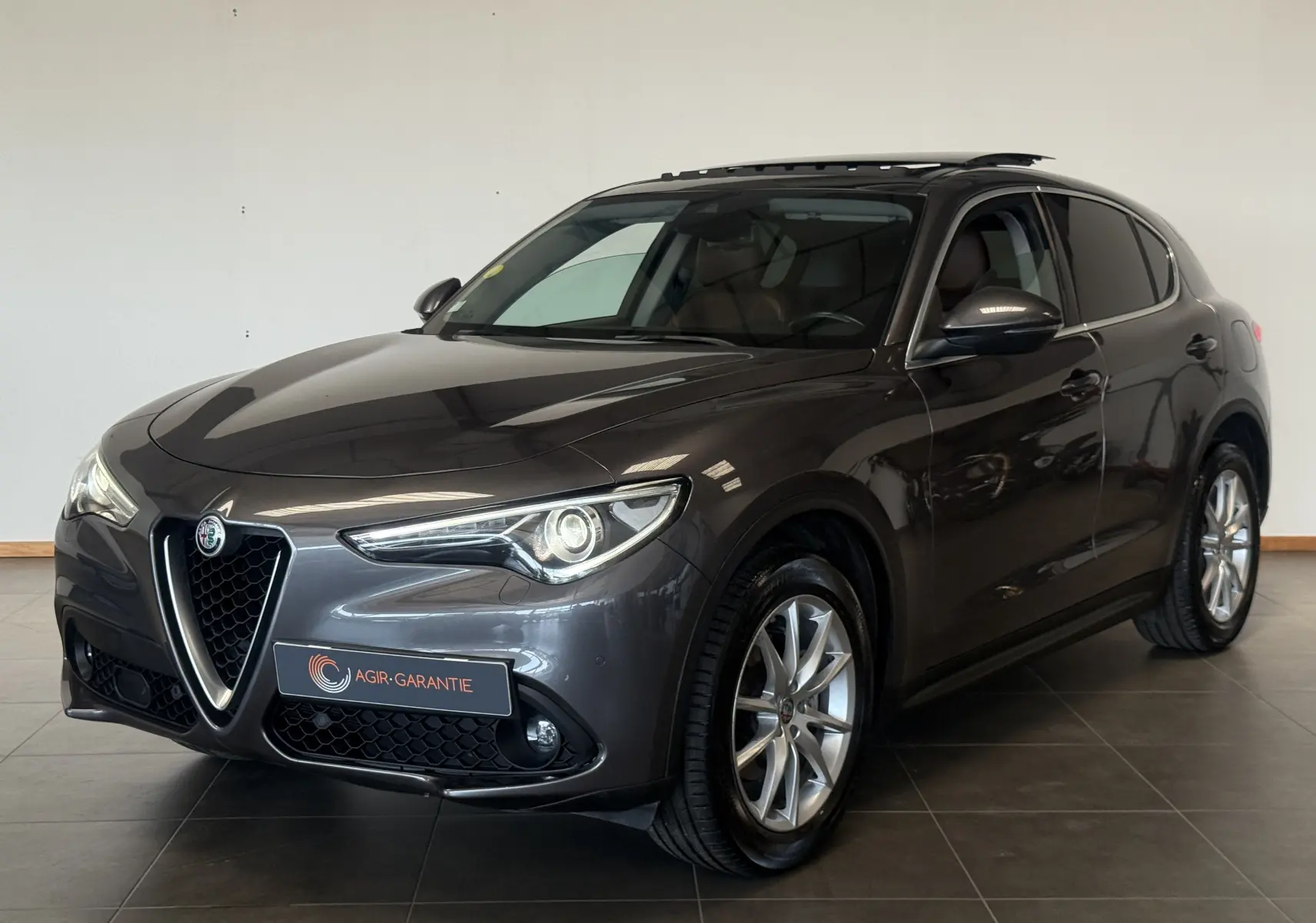 Alfa Romeo Stelvio gris vu de trois quarts avant droit, avec calandre caractéristique et jantes alliage.