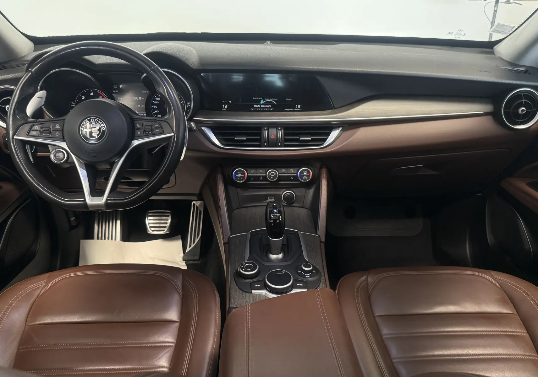 Vue intérieure de l'Alfa Romeo Stelvio 2017 avec tableau de bord noir, sièges cuir marron et console centrale bois.