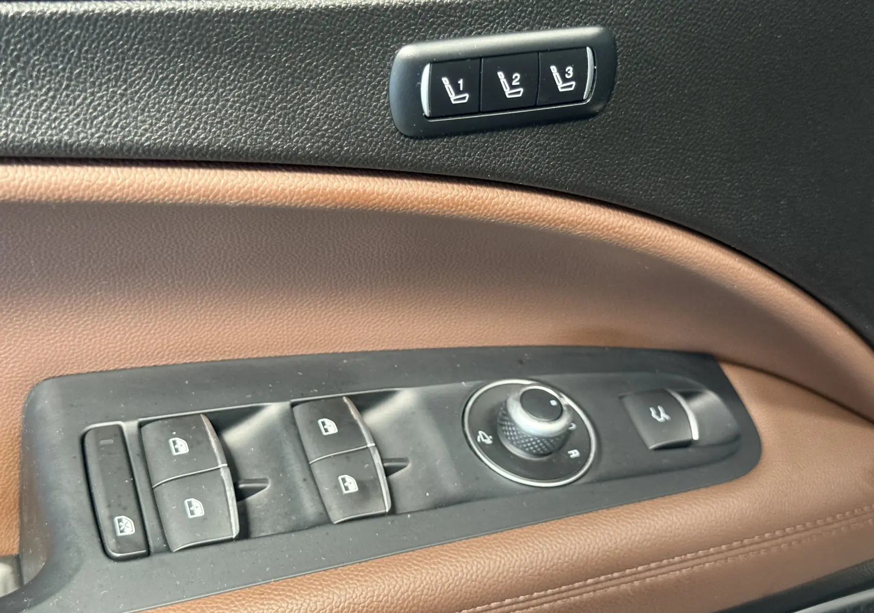 Gros plan sur les commandes de porte en cuir marron et noir de l'Alfa Romeo Stelvio 2017, incluant réglages des vitres et mémoires sièges.