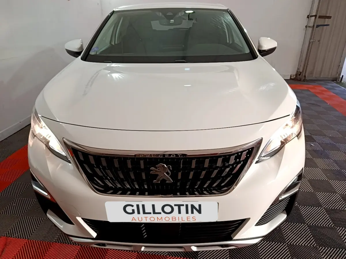 Vue avant d'un Peugeot 3008 blanc hybride rechargeable avec calandre noire et phares allumés dans un garage.