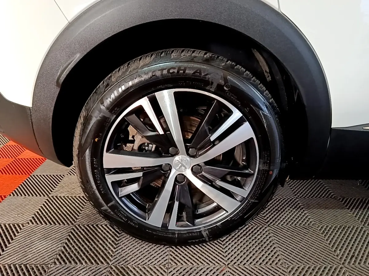 Gros plan sur la roue avant gauche du Peugeot 3008 blanc, mettant en valeur la jante alliage bicolore et le pneu.