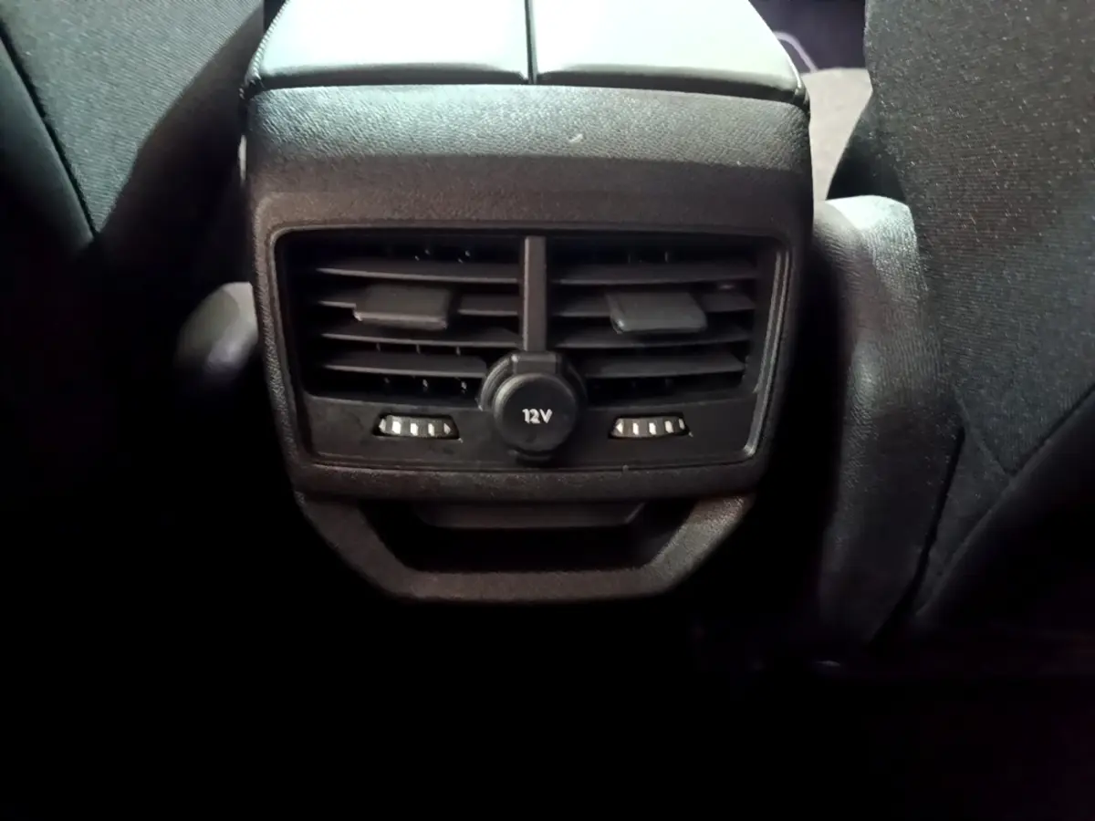 Gros plan sur la sortie d’air arrière noire avec prise 12V du Peugeot 3008 hybride rechargeable blanc, intérieur sombre.