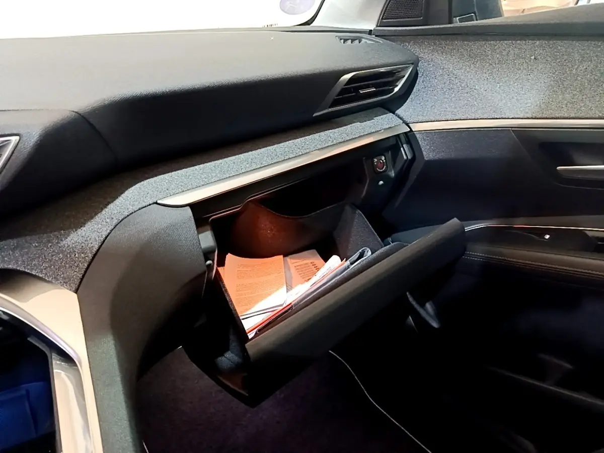 Intérieur côté passager du Peugeot 3008 hybride blanc, boîte à gants ouverte avec documents visibles, tableau de bord moderne.