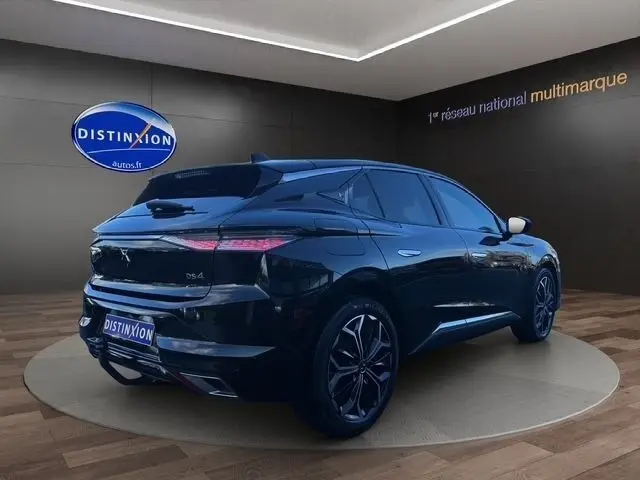 Vue 3/4 arrière d'une DS4 noire 2022 avec spoiler de coffre et feux arrière LED, en showroom intérieur.