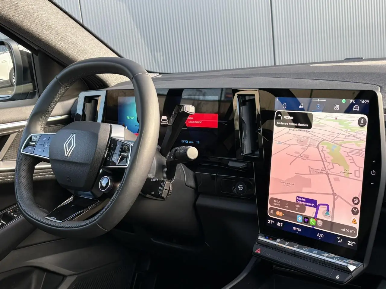 Vue intérieure côté conducteur du tableau de bord noir avec grand écran tactile vertical et volant Renault moderne.