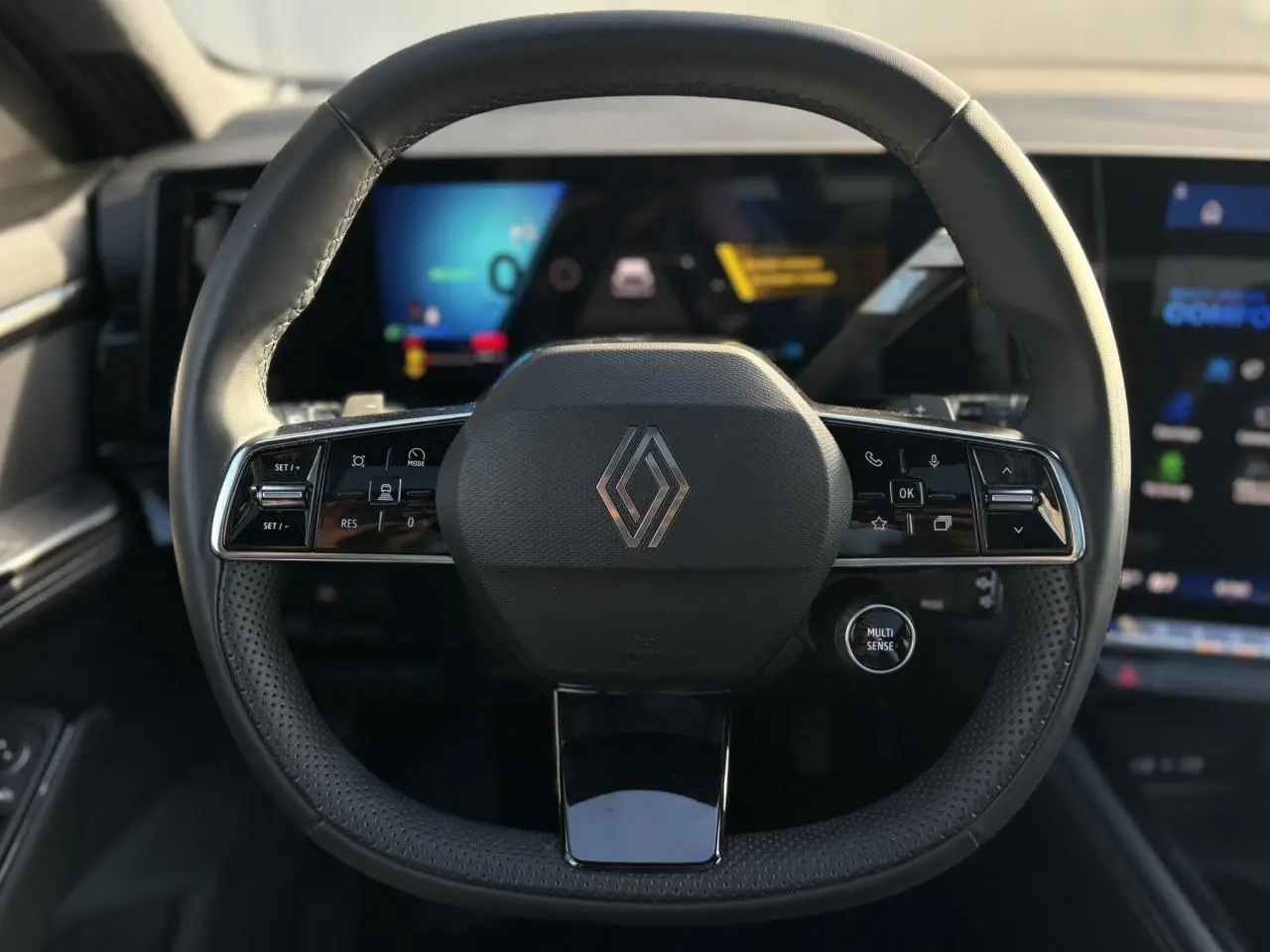 Vue rapprochée du volant noir perforé du Renault Austral 2025 avec commandes intégrées et tableau de bord numérique en arrière-plan.
