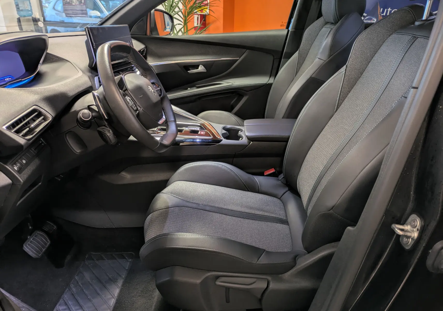 Vue intérieure côté conducteur du Peugeot 5008 noir 2024, mettant en valeur la sellerie TEP et tissu et le volant cuir.