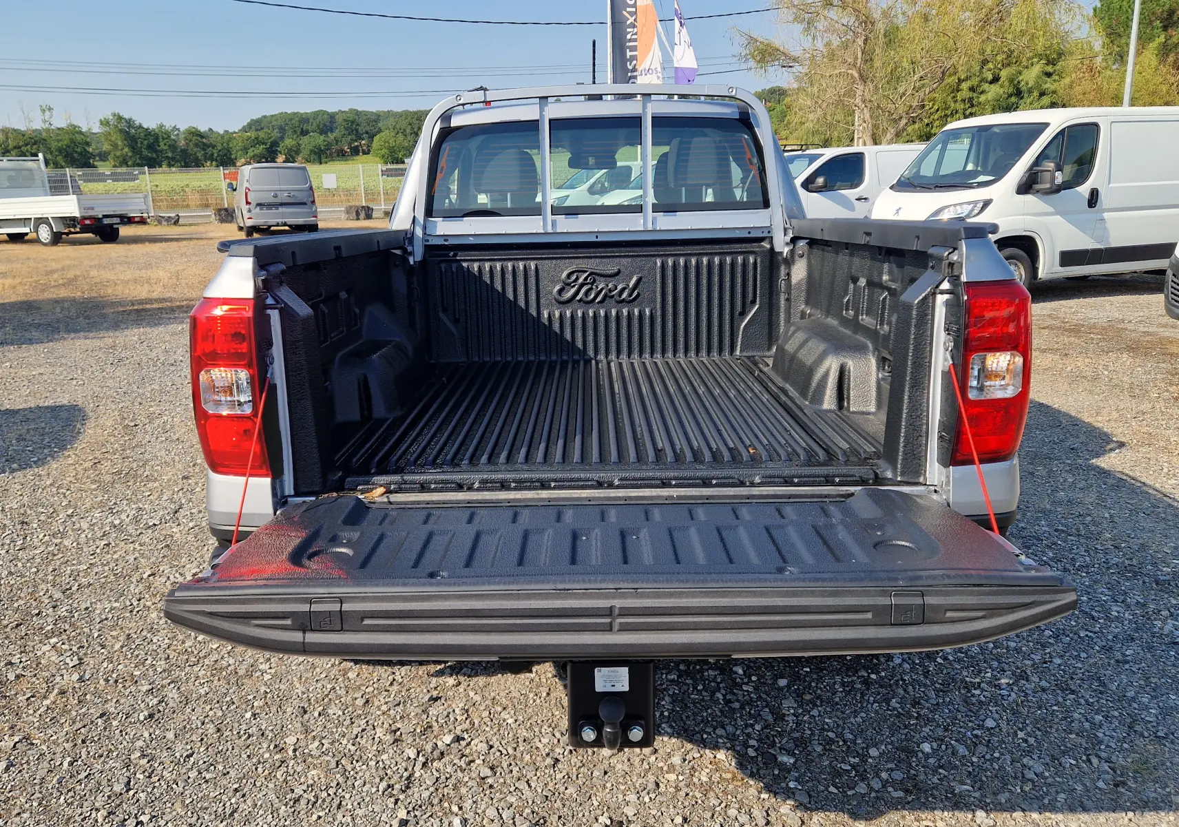 Vue arrière du Ford Ranger Super Cabine gris Iconic 2026 avec benne ouverte et hayon abaissé sur un parking extérieur.