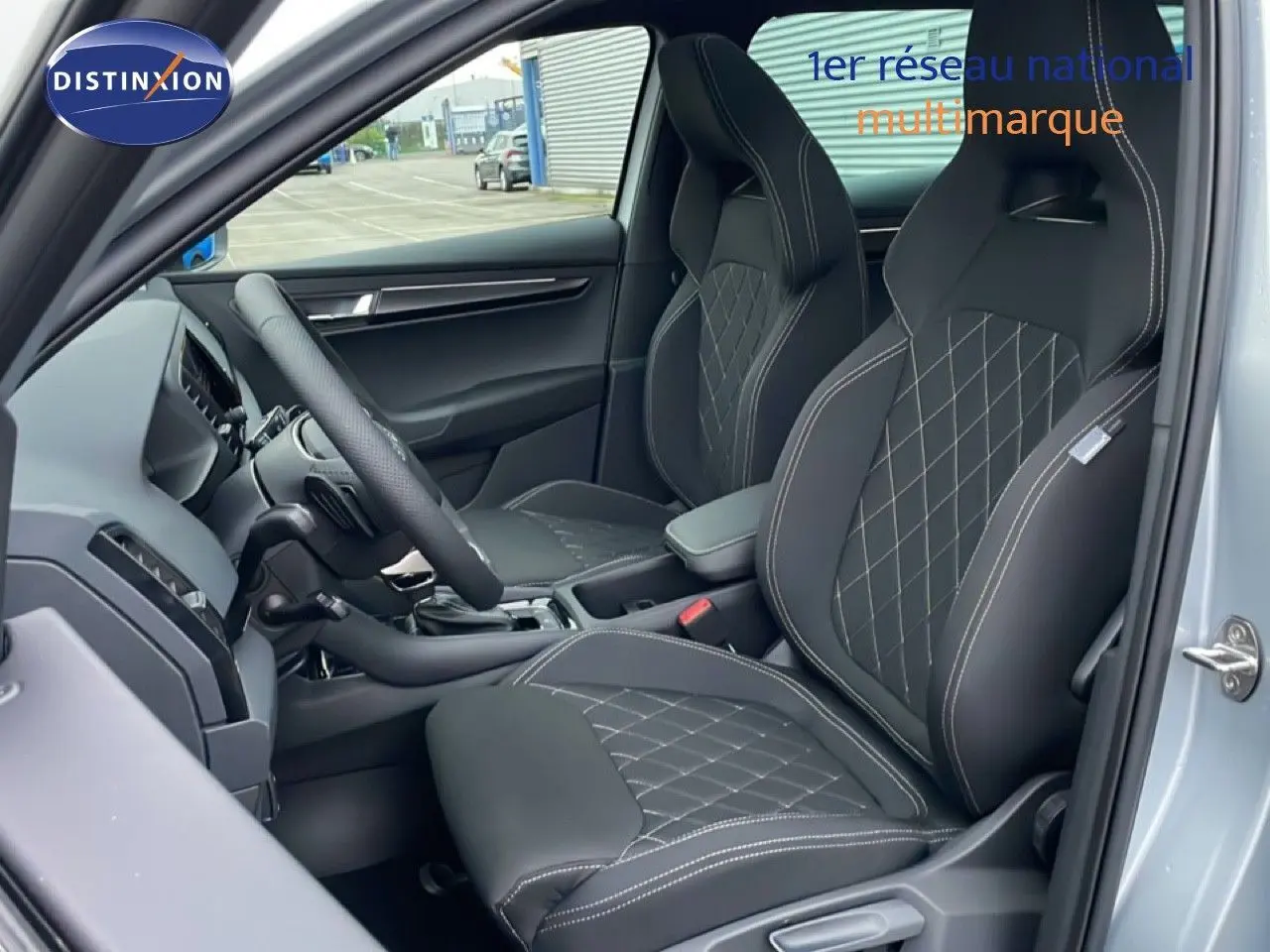 Vue intérieure côté conducteur du Skoda Karoq gris argent 2025, mettant en valeur les sièges sport noirs avec surpiqûres contrastées.