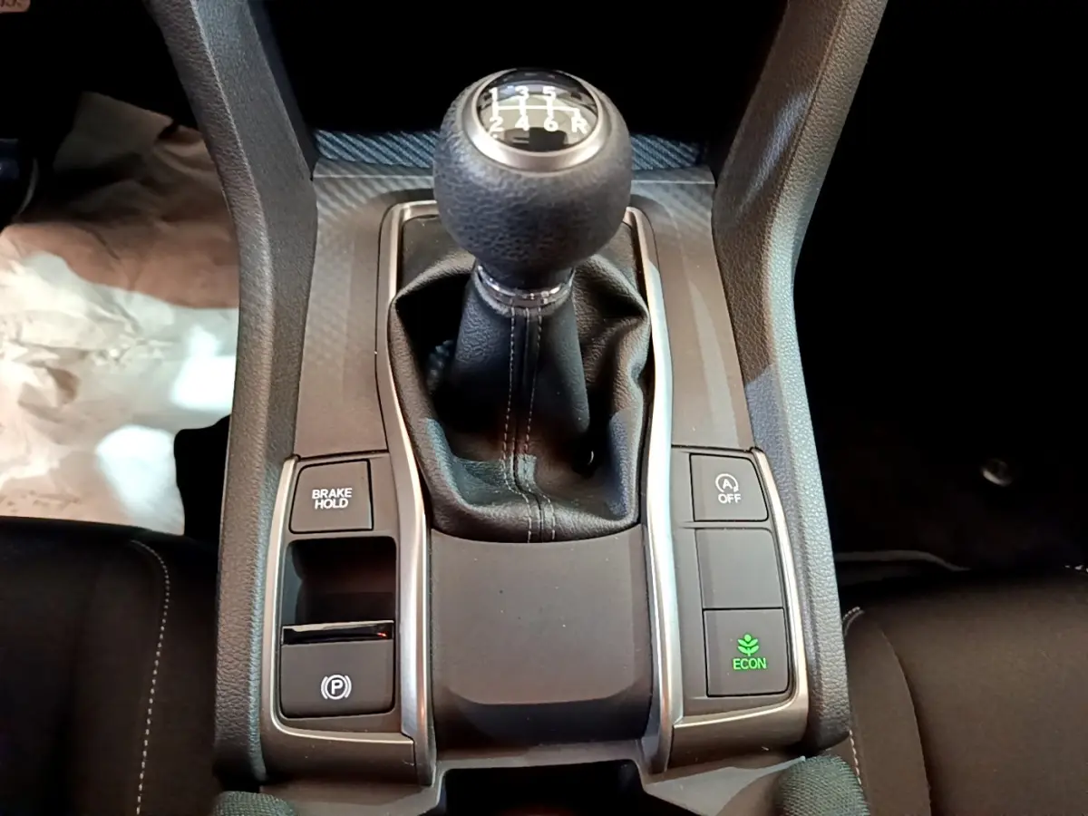 Vue rapprochée du levier de vitesses manuel noir et des boutons de contrôle sur la console centrale d'une Honda Civic gris foncé.