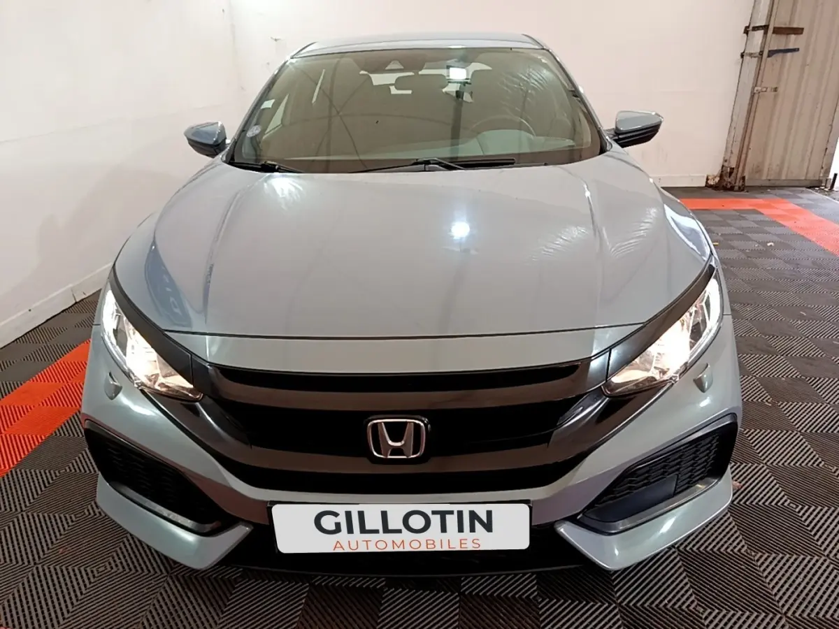 Vue avant frontale d'une Honda Civic 1.0 i-VTEC Exclusive gris foncé avec phares allumés dans un garage.