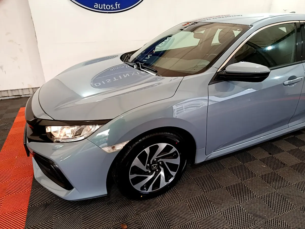 Vue 3/4 avant droit d'une Honda Civic 1.0 i-VTEC Exclusive gris foncé avec jantes alliage et phares allumés.