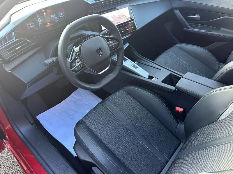 Vue intérieure côté conducteur de la Peugeot 308 SW 2024 Rouge Elixir, avec volant compact et écran tactile central.