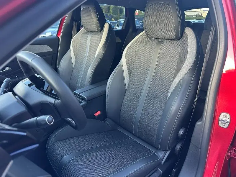 Vue intérieure côté conducteur de la Peugeot 308 SW 2024 rouge Elixir, mettant en valeur les sièges avant en tissu et cuir.