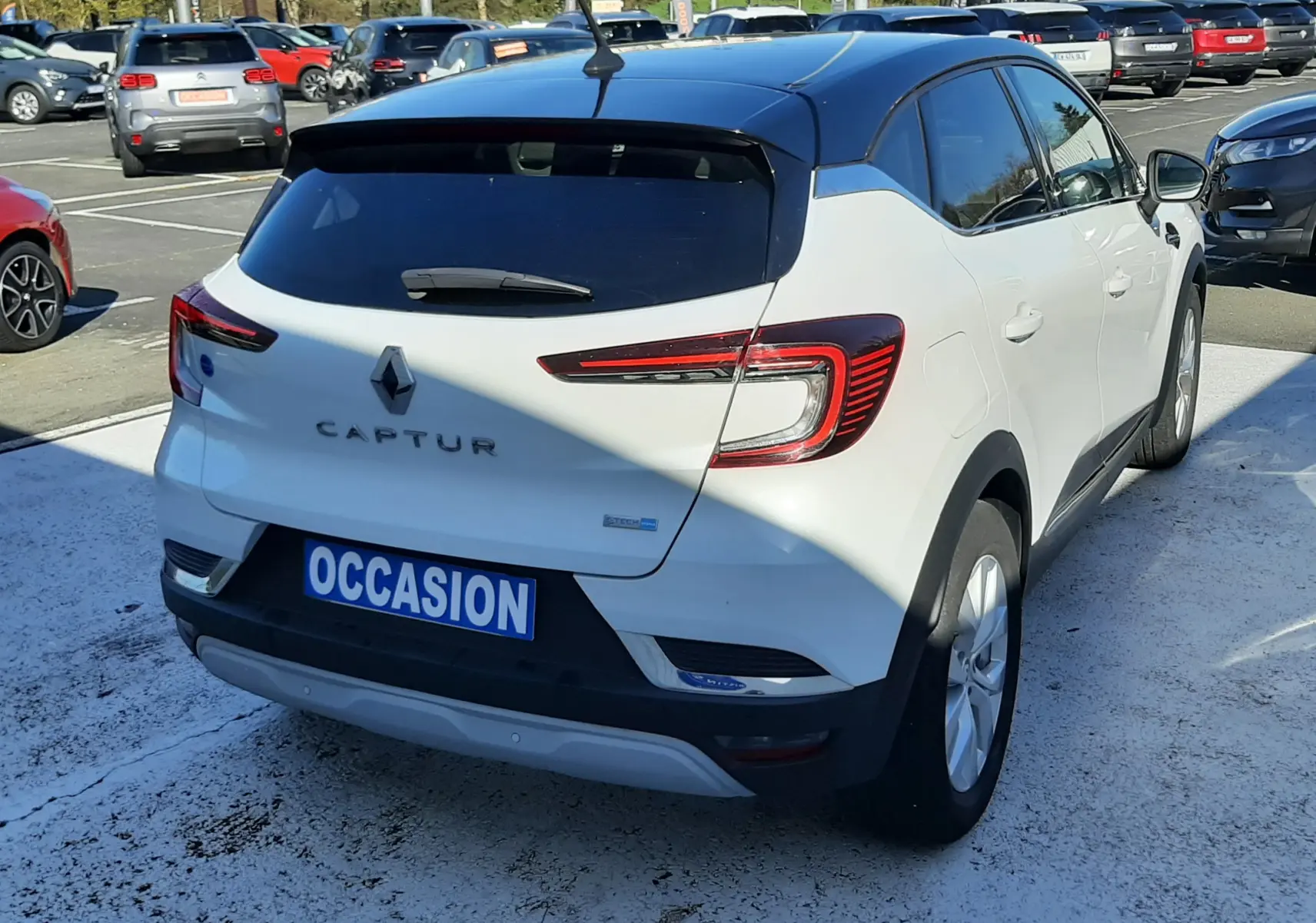 Vue 3/4 arrière droite du Renault Captur blanc nacré avec toit noir, sur parking en extérieur, plaque occasion visible.