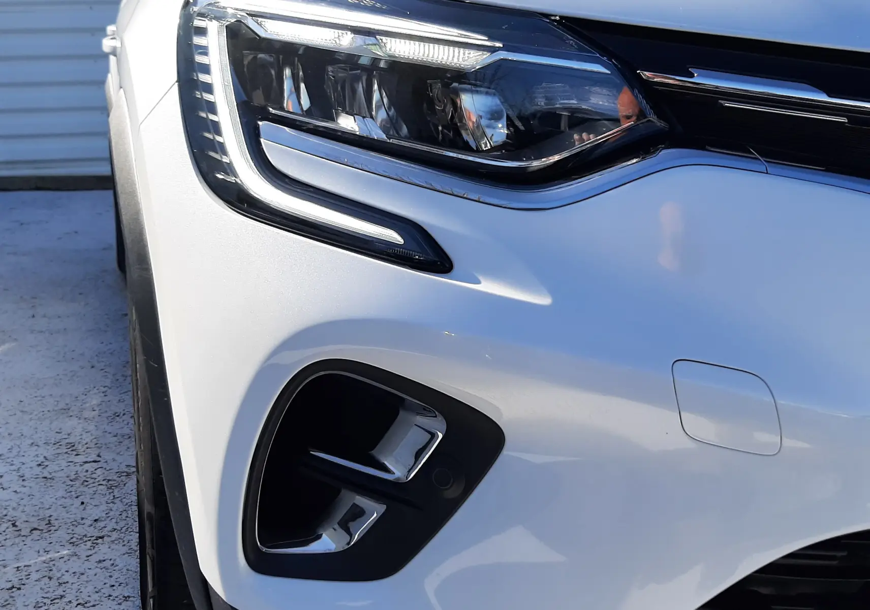 Gros plan sur l'avant gauche du Renault Captur E-Tech blanc nacré avec toit noir, mettant en valeur le phare LED et la calandre.