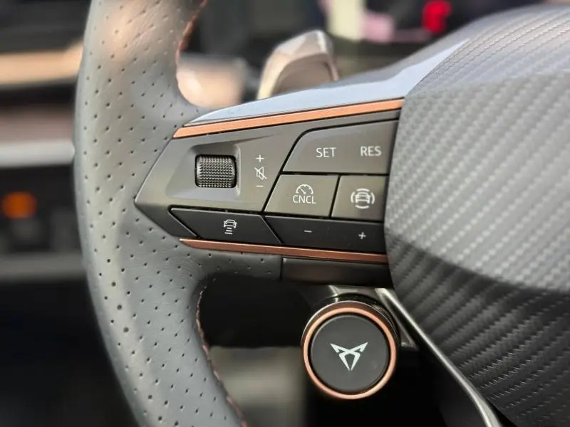 Gros plan sur les commandes gauche du volant perforé gris du CUPRA Formentor 2.0 TDI 150ch avec détails cuivre et logo central.