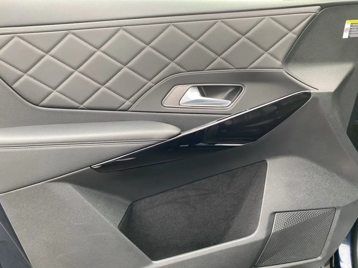 Gros plan sur la porte intérieure côté droit du DS7 Crossback 2024, avec cuir matelassé gris et insert noir brillant.