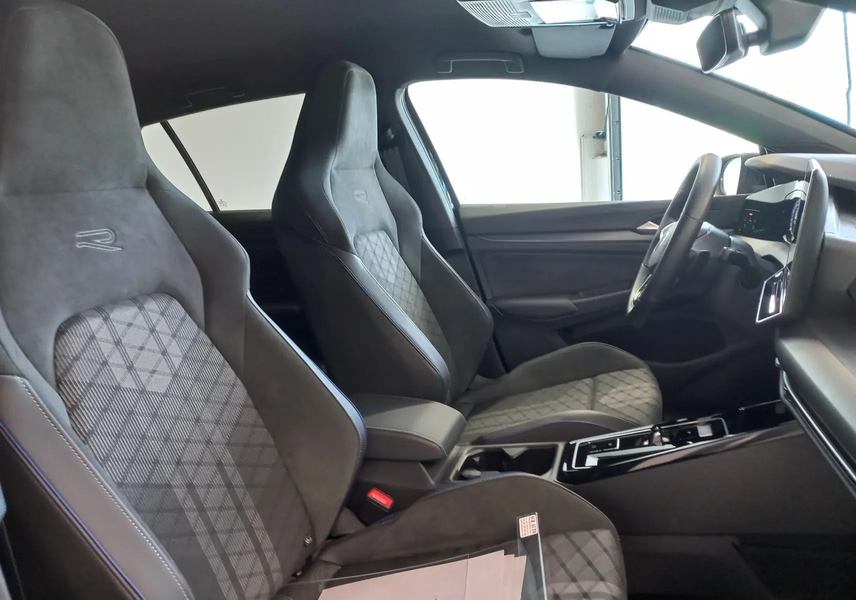 Vue intérieure côté conducteur de la Volkswagen Golf 1.5 eTSI R-Line 2025 avec sièges sport en tissu noir et tableau de bord moderne.