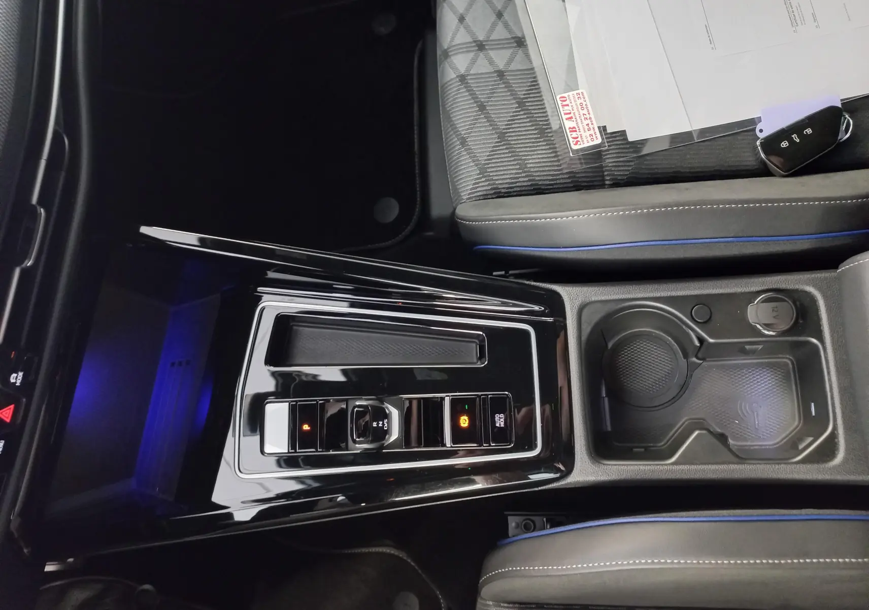 Vue plongeante sur la console centrale noire brillante de la Volkswagen Golf 1.5 eTSI 2025 avec accoudoirs et porte-gobelets.