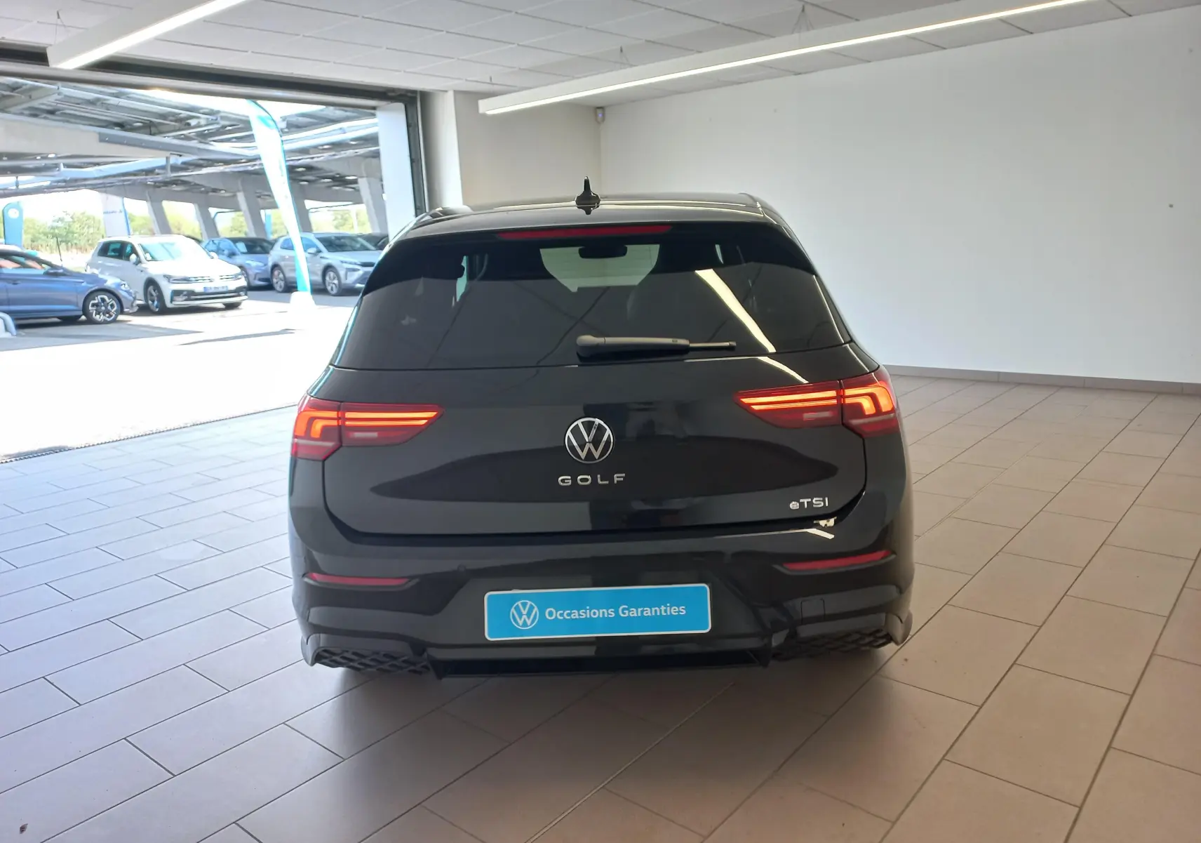 Vue arrière d'une Volkswagen Golf 1.5 eTSI 150 DSG7 R-Line Edition noir ébène en intérieur, feux LED allumés.