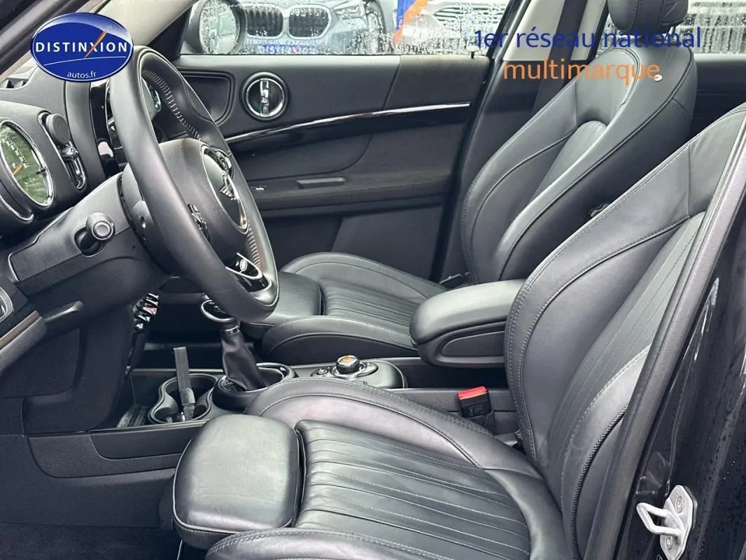 Vue intérieure côté conducteur du MINI Countryman noir, mettant en valeur les sièges cuir et l'accoudoir central.