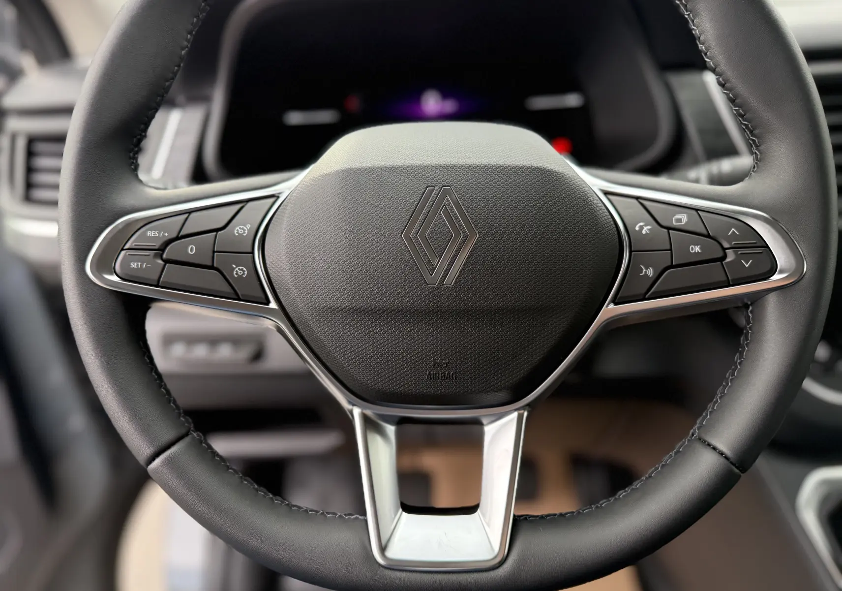 Gros plan sur le volant noir du Renault Trafic Combi 2025 avec commandes intégrées et logo central chromé.