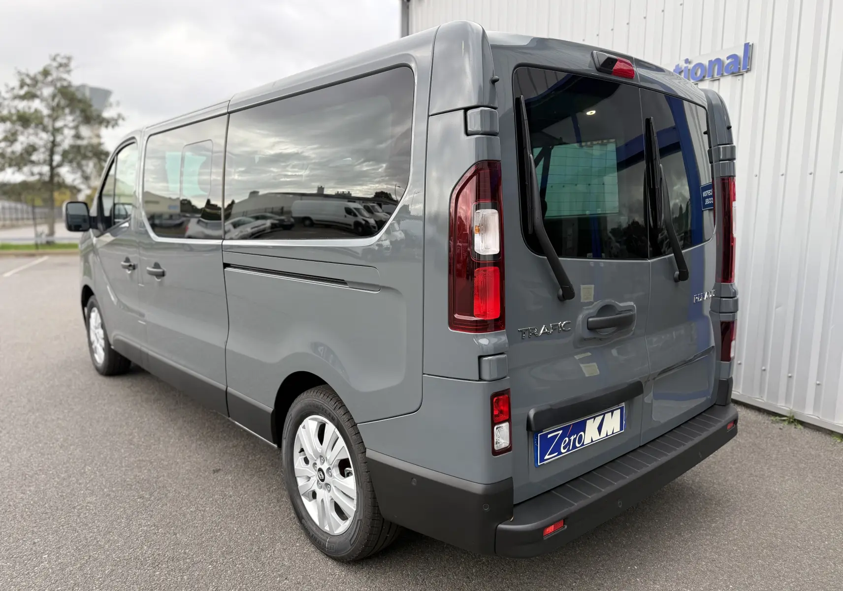 Renault Trafic Combi gris urbain vu en 3/4 arrière droit, avec vitres teintées et feux arrière verticaux.