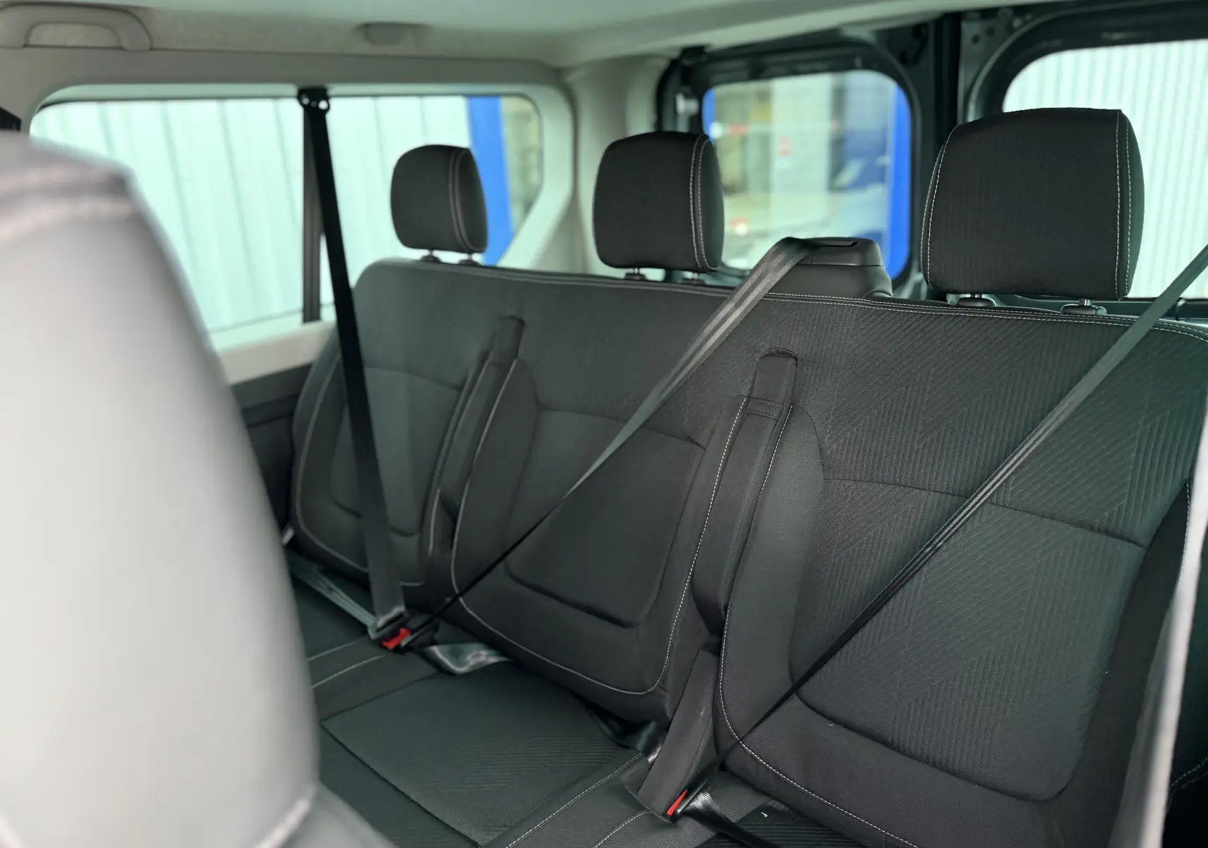 Vue intérieure arrière du Renault Trafic Combi gris urbain 2025, montrant les sièges en tissu noir avec ceintures attachées.